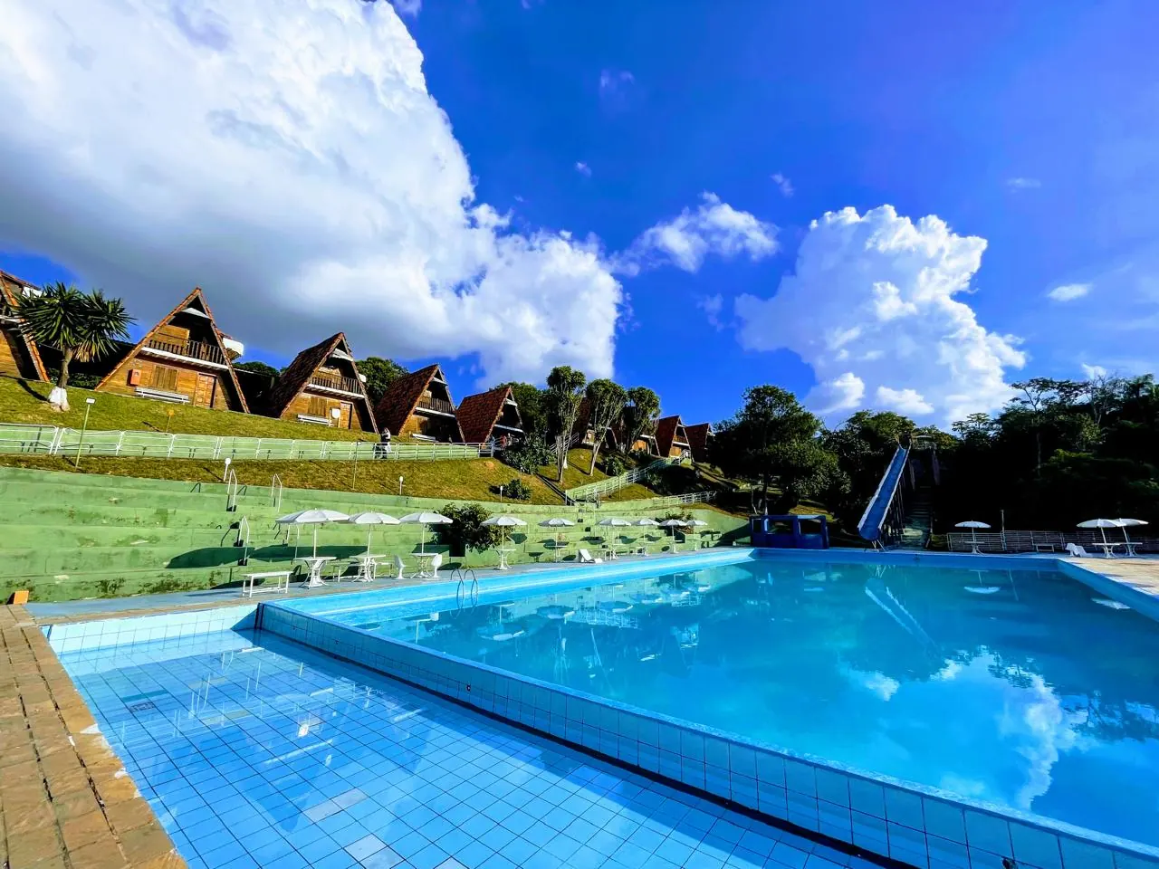 Chalés no alto do gramado com a piscina à frente